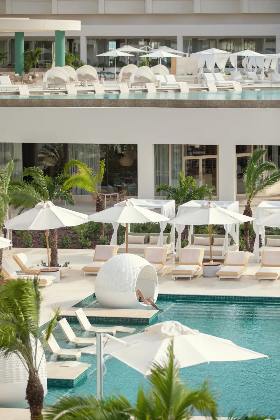 Poolside umbrellas, loungers, palms, and a round shaded daybed at JOIA Aruba.