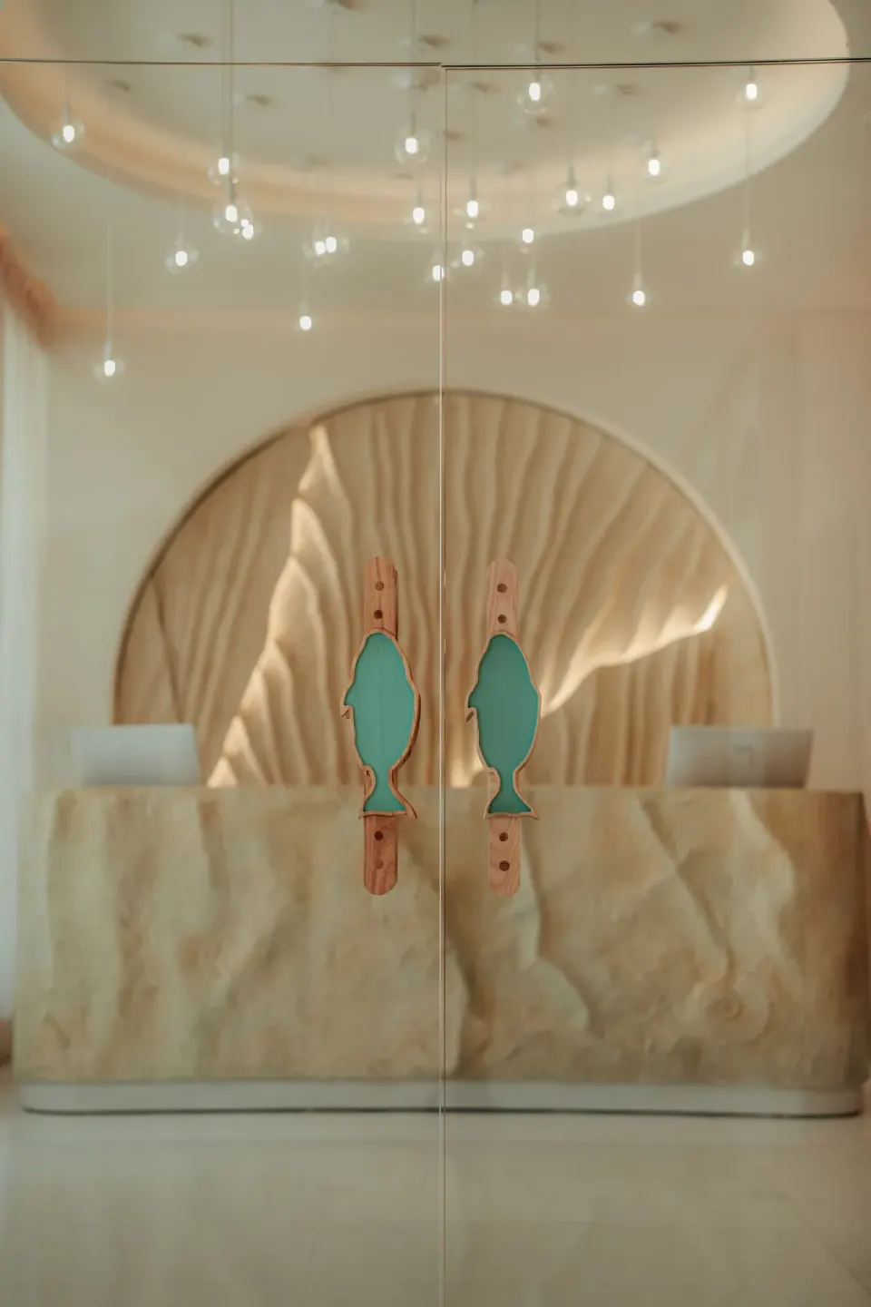 Glass doors with fish-shaped handles open to a softly lit reception desk at JOIA Aruba.