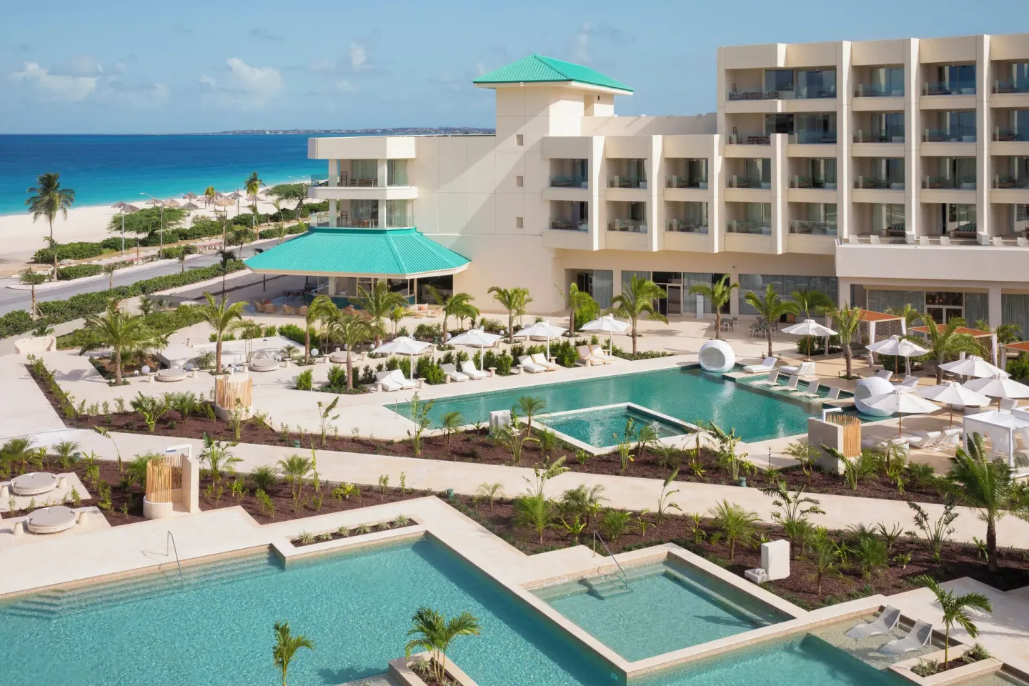 Wide resort view with pools, palms, beach, and turquoise ocean at JOIA Aruba.