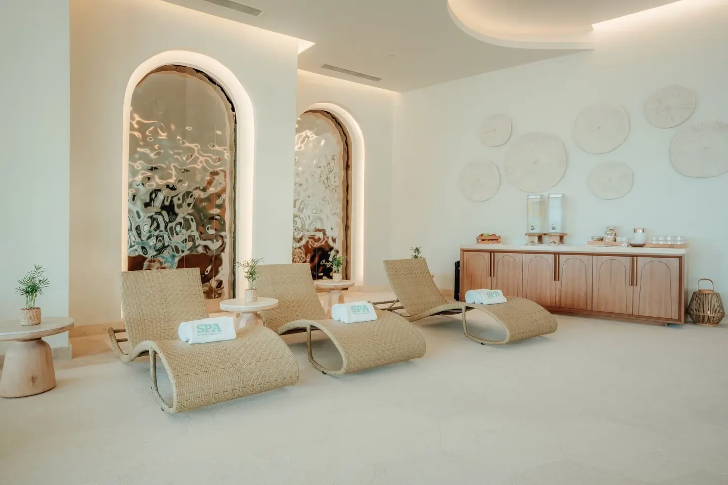 Spa lounge with woven chaise lounges, towels, and refreshment counter at JOIA Aruba.