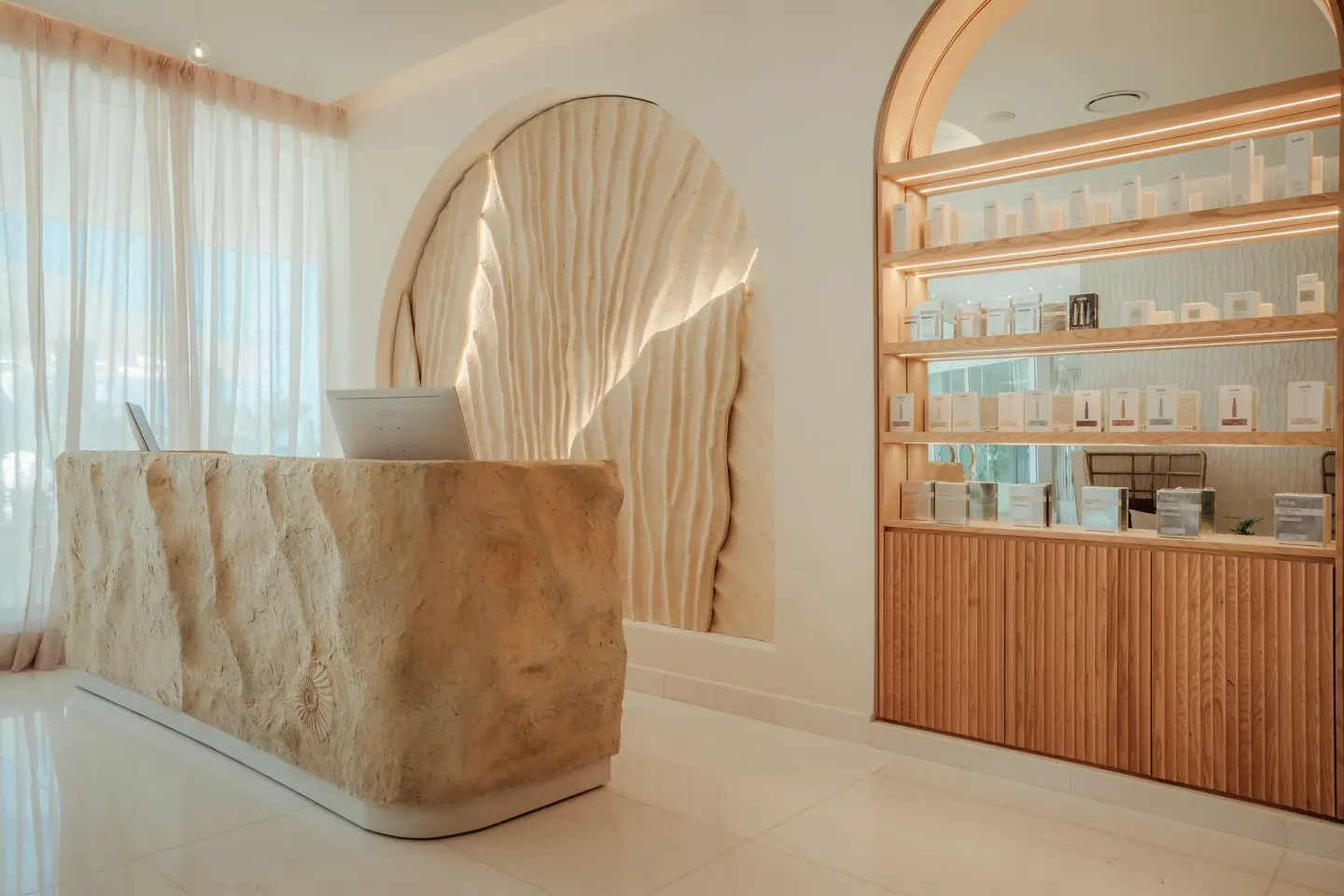 Spa reception desk with retail shelves and shell-inspired wall feature at JOIA Aruba.