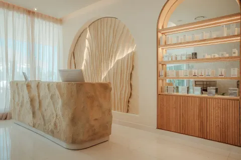 Spa reception desk with retail shelves and shell-inspired wall feature at JOIA Aruba.