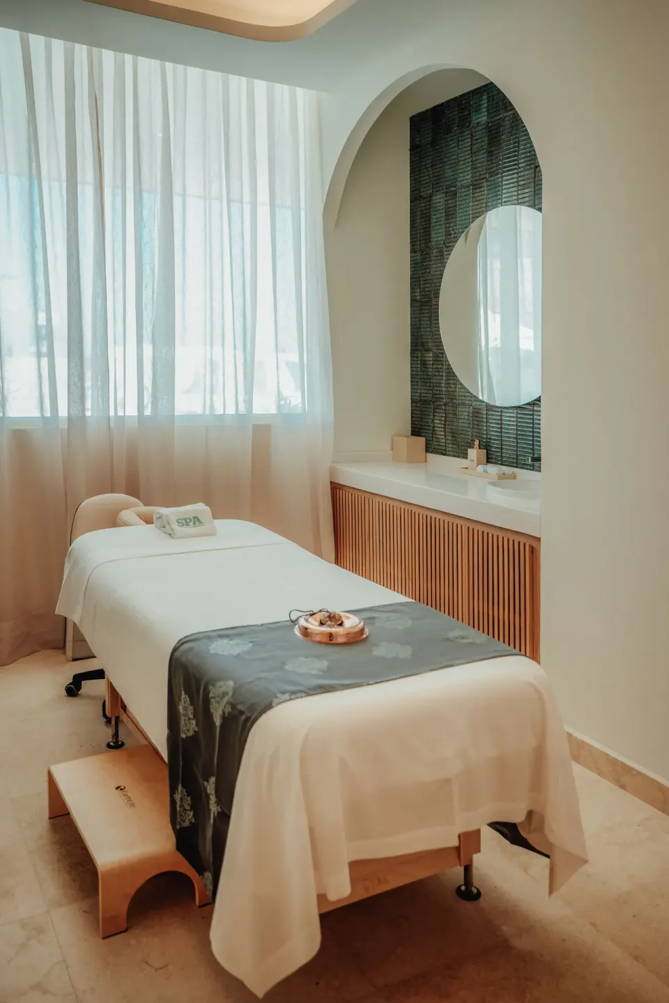 Single spa treatment bed with a round mirror and sheer curtains at JOIA Aruba.