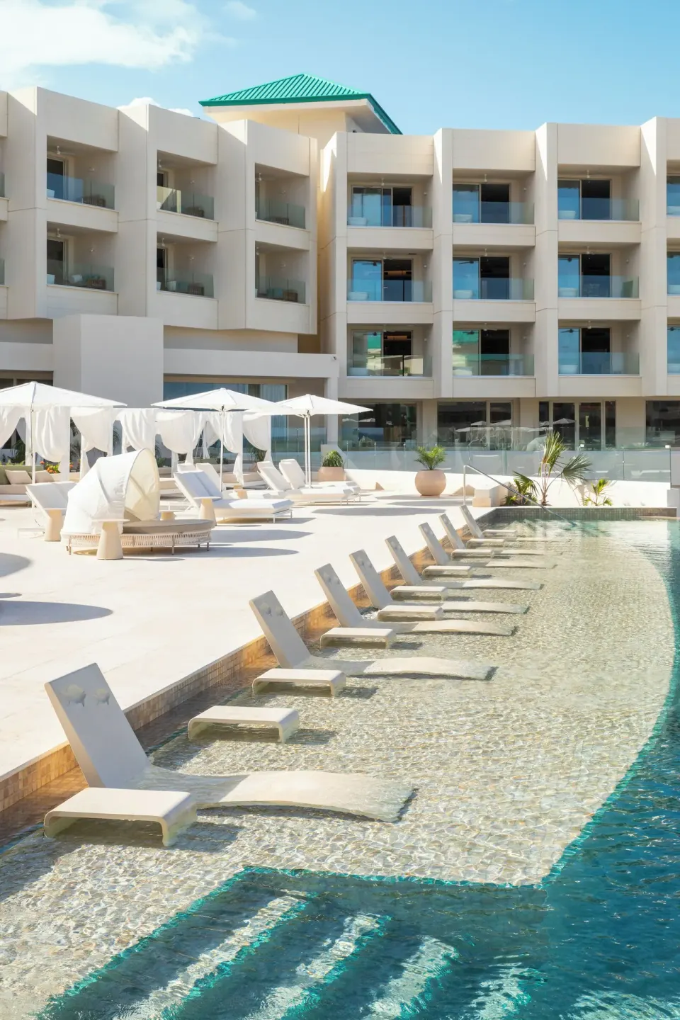 Shallow pool shelf with submerged loungers facing the resort building at JOIA Aruba.