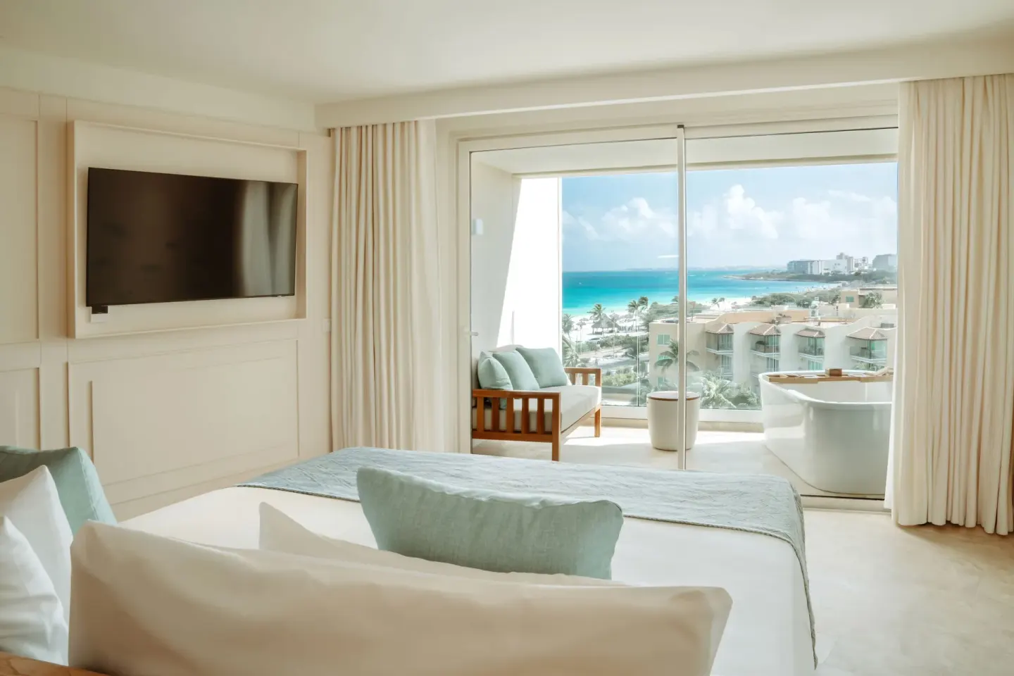 Suite Ocean View bedroom at JOIA Aruba with balcony seating, freestanding tub and sea view.