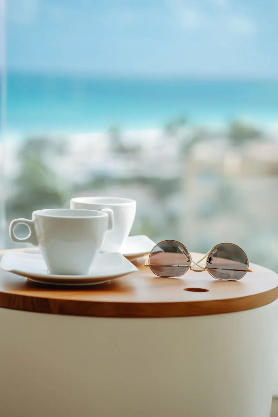 Coffee cups and sunglasses on a balcony table in the Pool View Suite at JOIA Aruba.