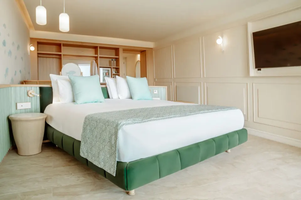 Pool View Suite bedroom with king bed, mint accents, and wall-mounted TV at JOIA Aruba.