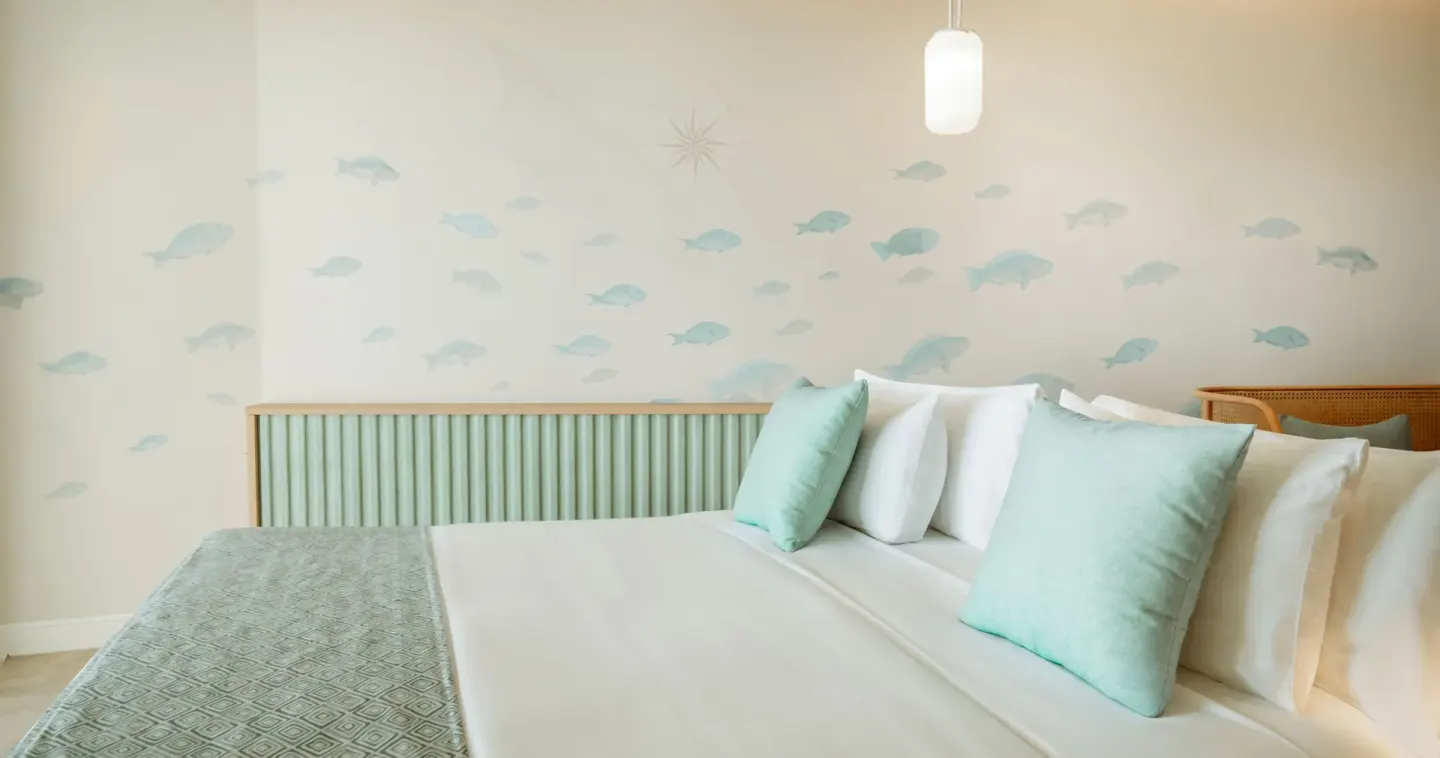 Pool View Suite king bed with fish-pattern wall art and aqua pillows at JOIA Aruba.
