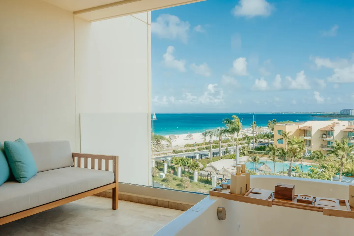 Suite balcony seating and soaking tub with side ocean view at JOIA Aruba.