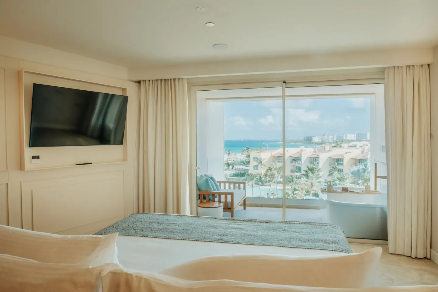 Suite bedroom with king bed, wall TV, balcony, and side ocean view at JOIA Aruba.