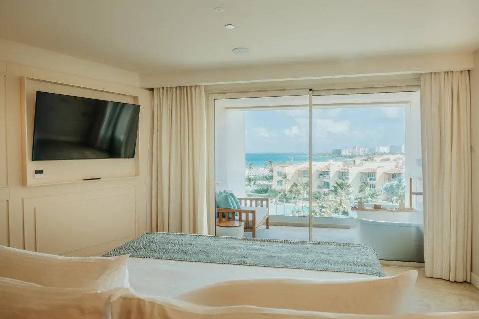 Suite bedroom with king bed, wall TV, balcony, and side ocean view at JOIA Aruba.