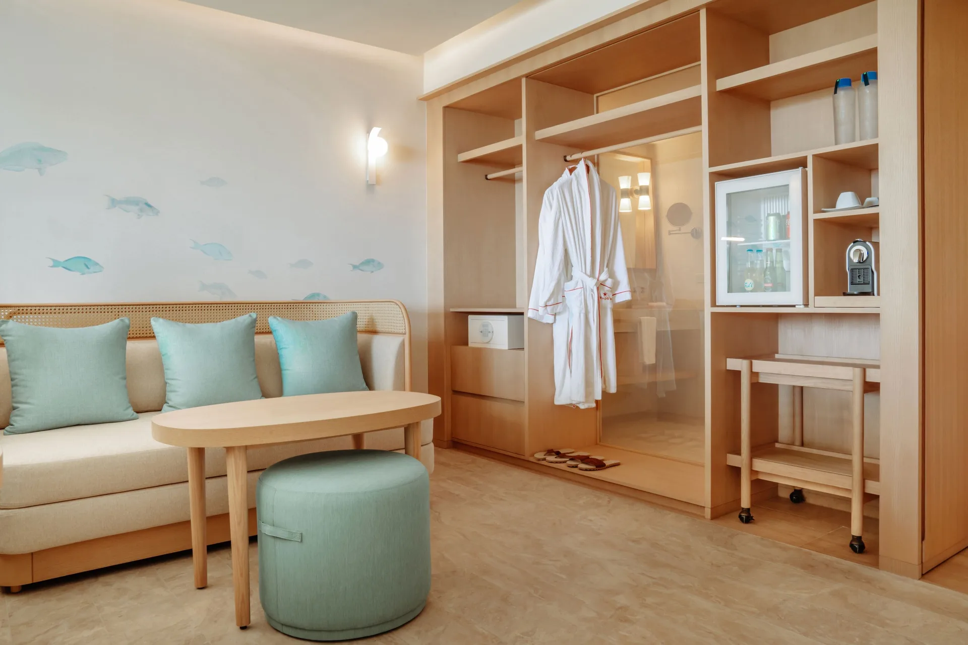 Suite sitting area with sofa, open wardrobe, robes and minibar at JOIA Aruba.