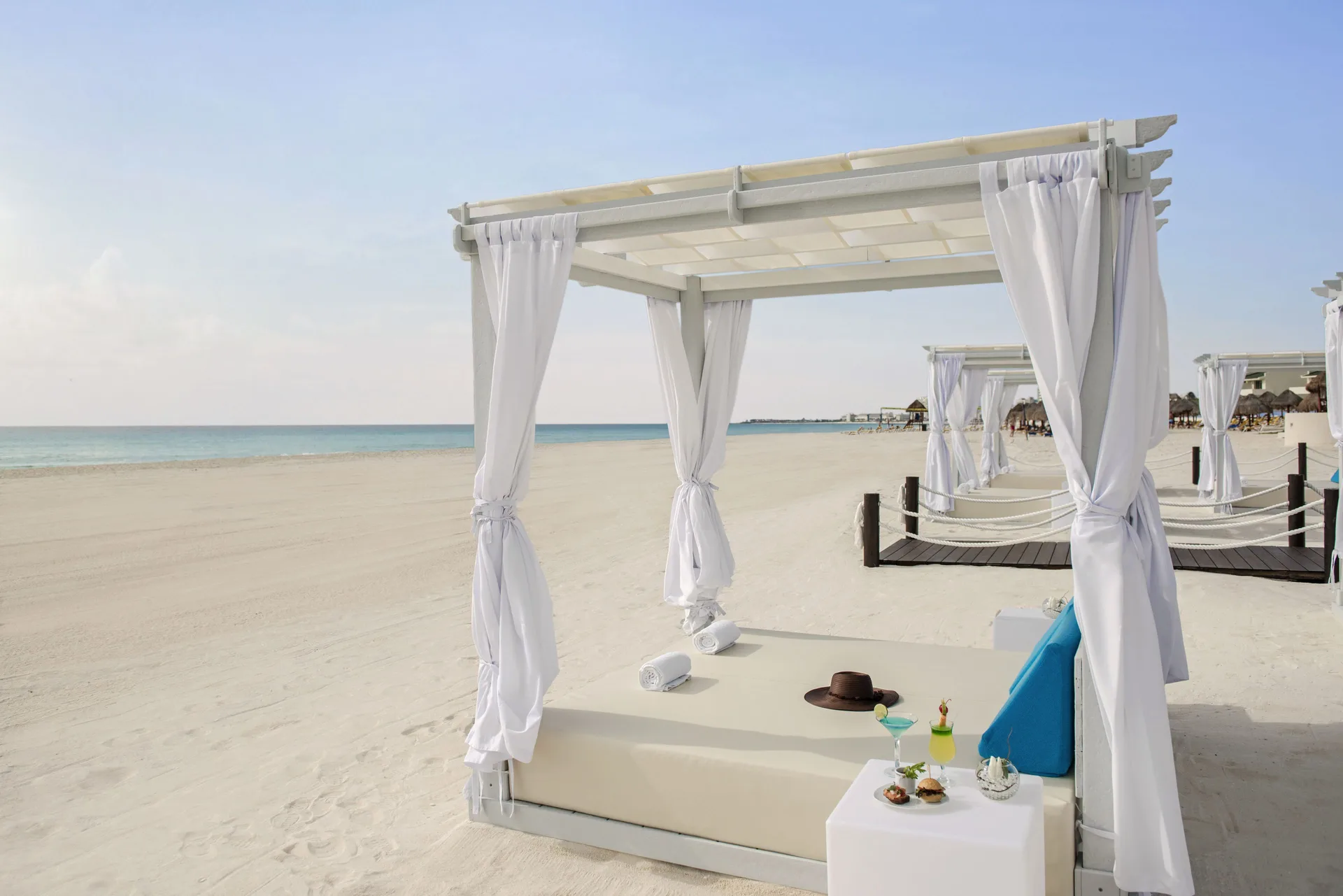 White curtained beach cabana with drinks and towels at JOIA Bávaro by Iberostar.