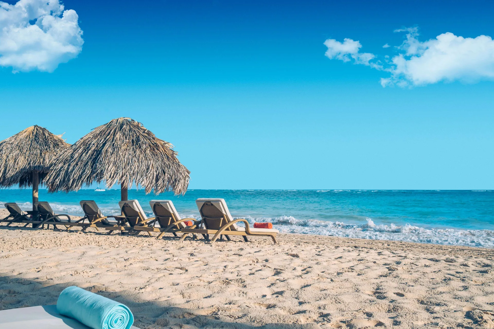 Beach loungers under thatched umbrellas beside the ocean at JOIA Bávaro by Iberostar.