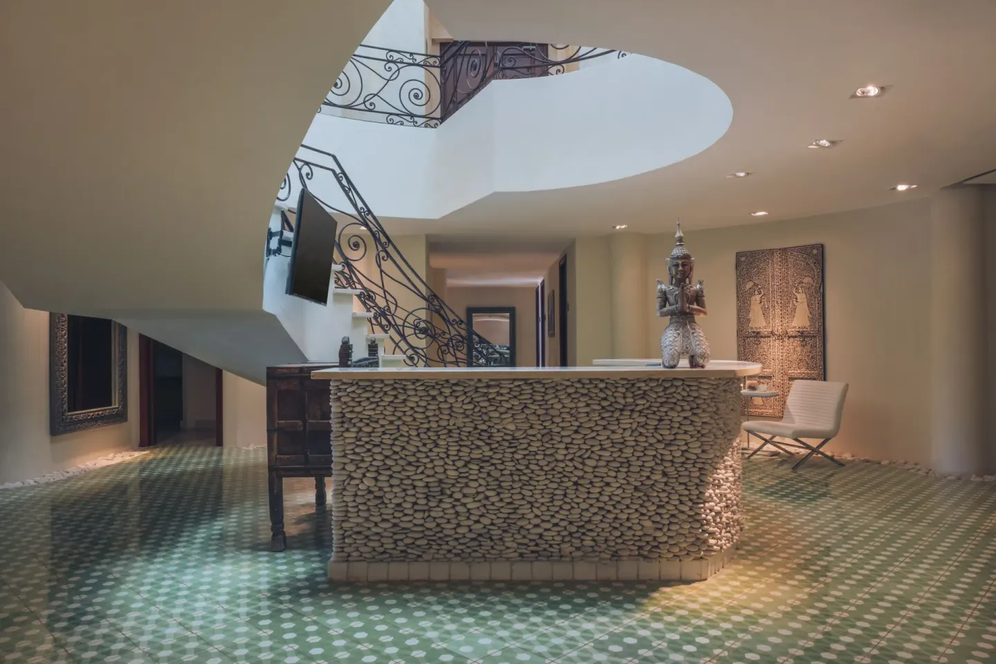 Curved lobby staircase and pebble-front desk at JOIA Bávaro by Iberostar.
