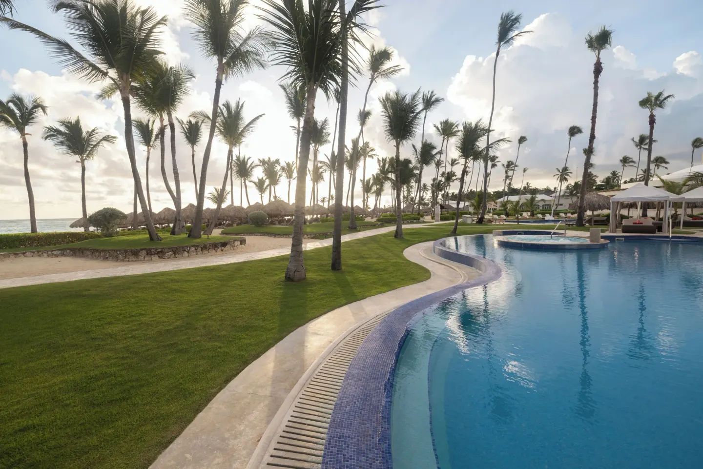 Curved pool beside palm lawns near the beach at JOIA Bávaro by Iberostar.