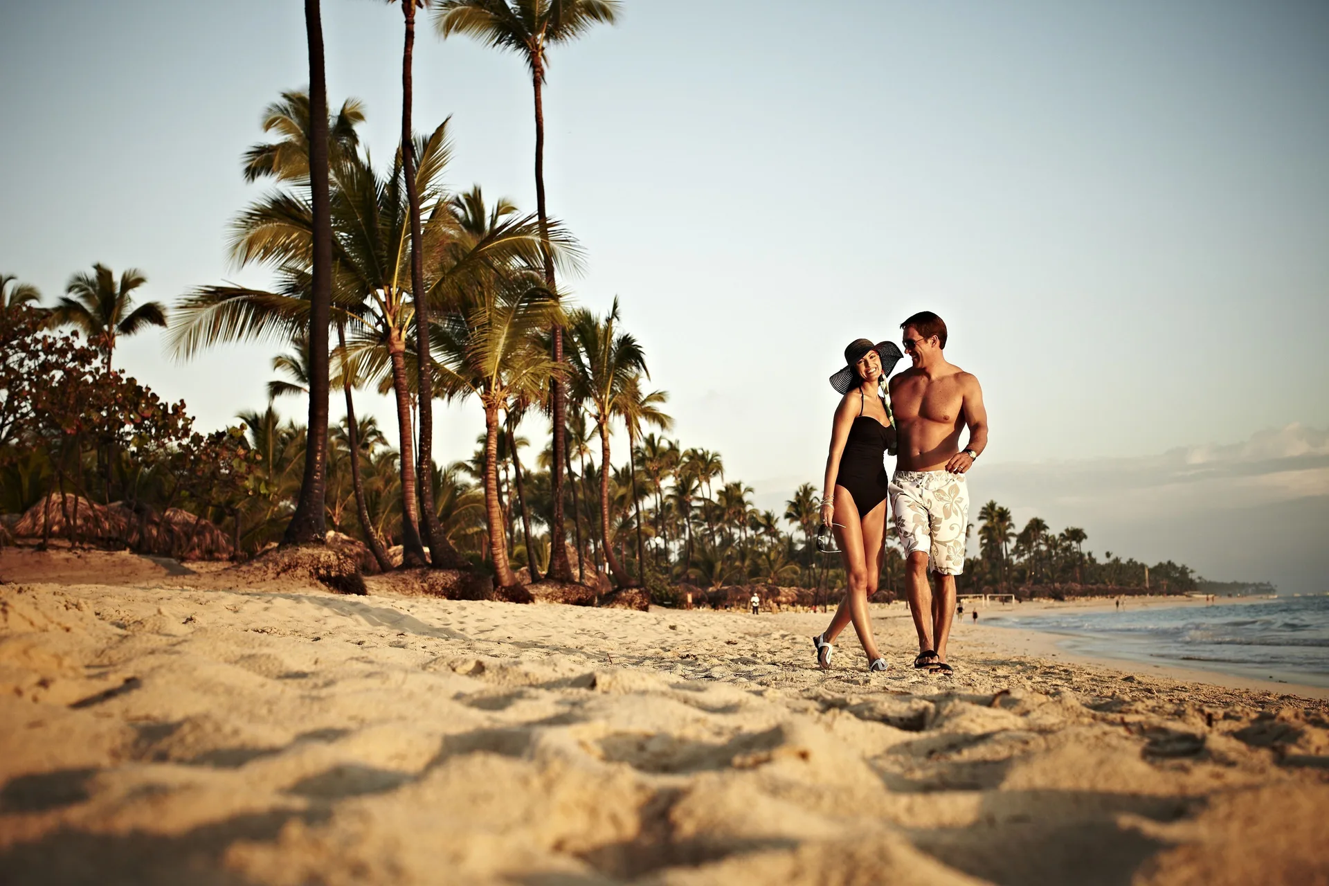 Couple walking along a palm-lined beach at JOIA Bávaro by Iberostar.