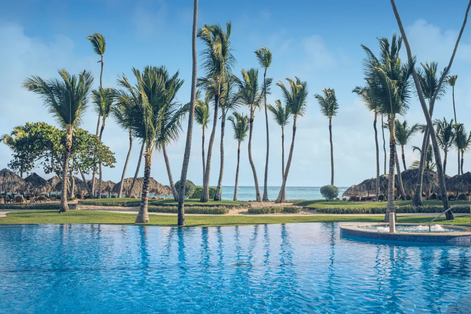Pool bordered by palms and ocean beyond at JOIA Bávaro by Iberostar.