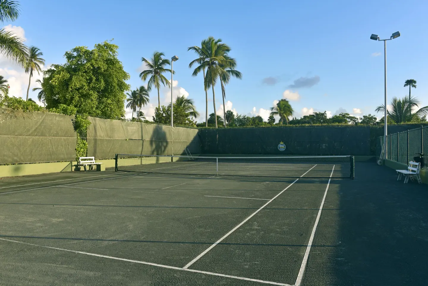 Tennis court with benches and palm trees at JOIA Bávaro by Iberostar.