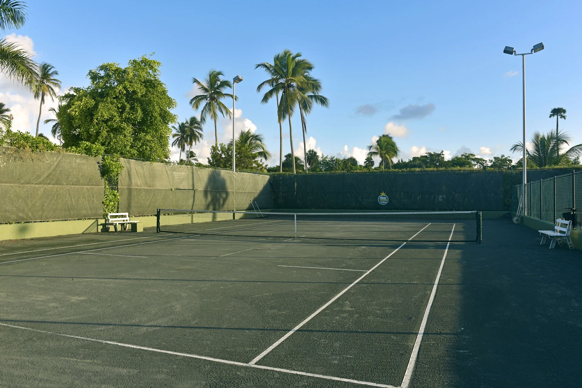 Tennis court with benches and palm trees at JOIA Bávaro by Iberostar.