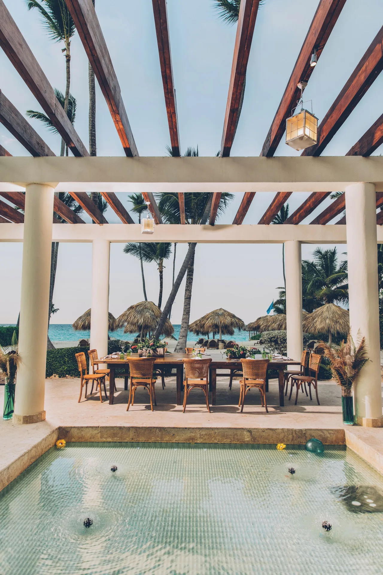 Pergola dining table by a shallow reflecting pool and beach at JOIA Bávaro by Iberostar.