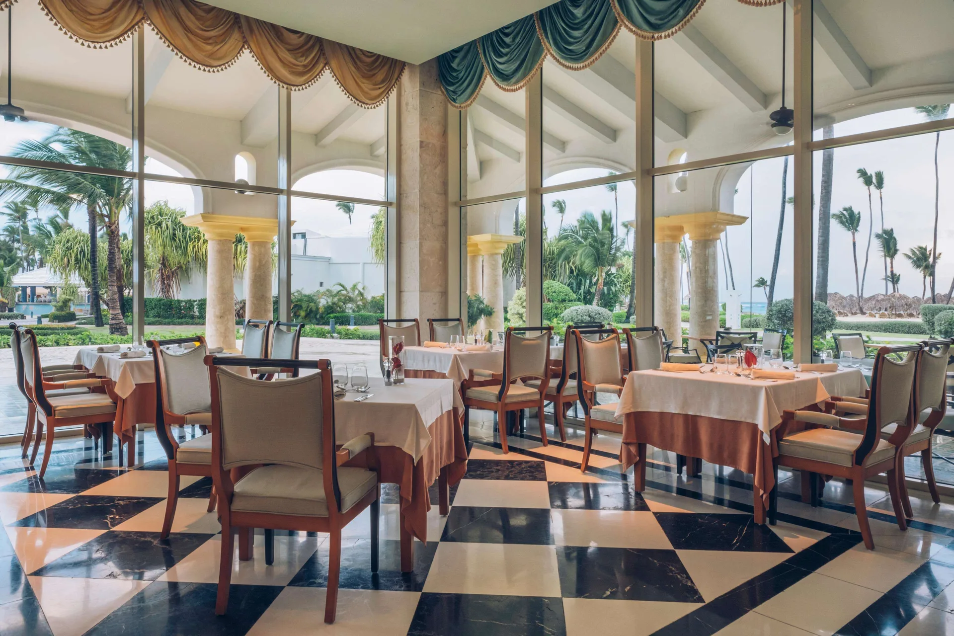 Window-lined dining room overlooking palms and gardens at JOIA Bávaro by Iberostar.