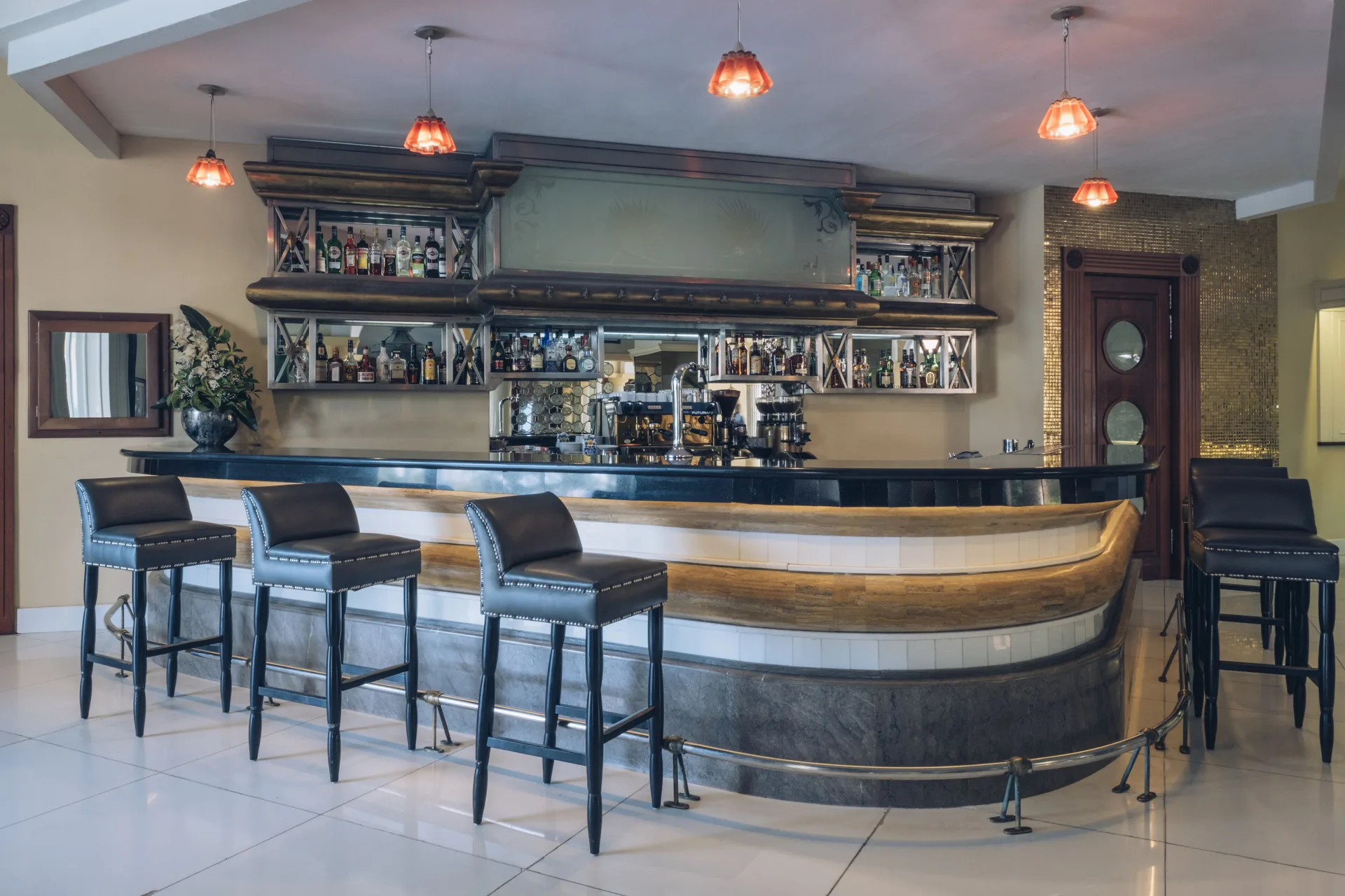 Indoor bar with curved counter, bottle shelves and black stools at JOIA Bávaro by Iberostar.
