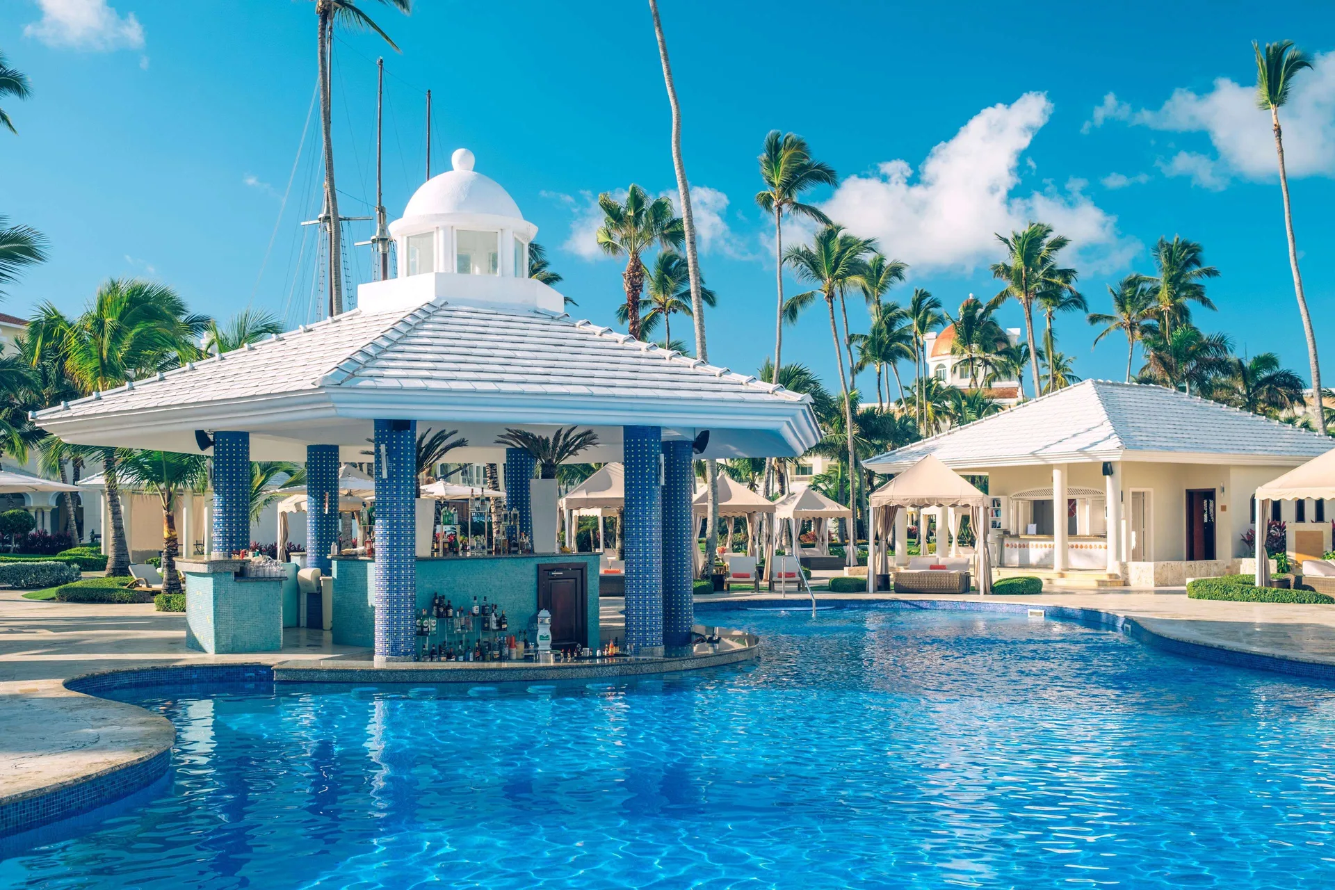 Swim-up pool bar with white roof and blue columns at JOIA Bávaro by Iberostar.