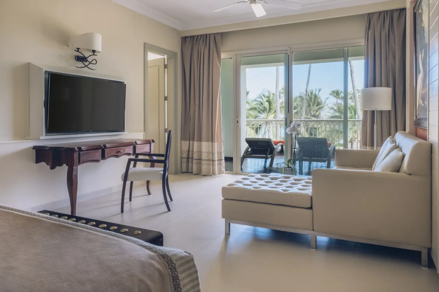 Oceanfront suite lounge with TV and balcony palms at JOIA Bávaro by Iberostar.