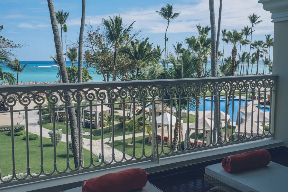 Oceanfront suite balcony view of beach, pool and palms at JOIA Bávaro by Iberostar.