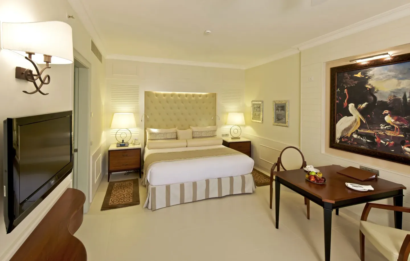 Suite bedroom with king bed, wall-mounted TV and dining table at JOIA Bávaro by Iberostar.