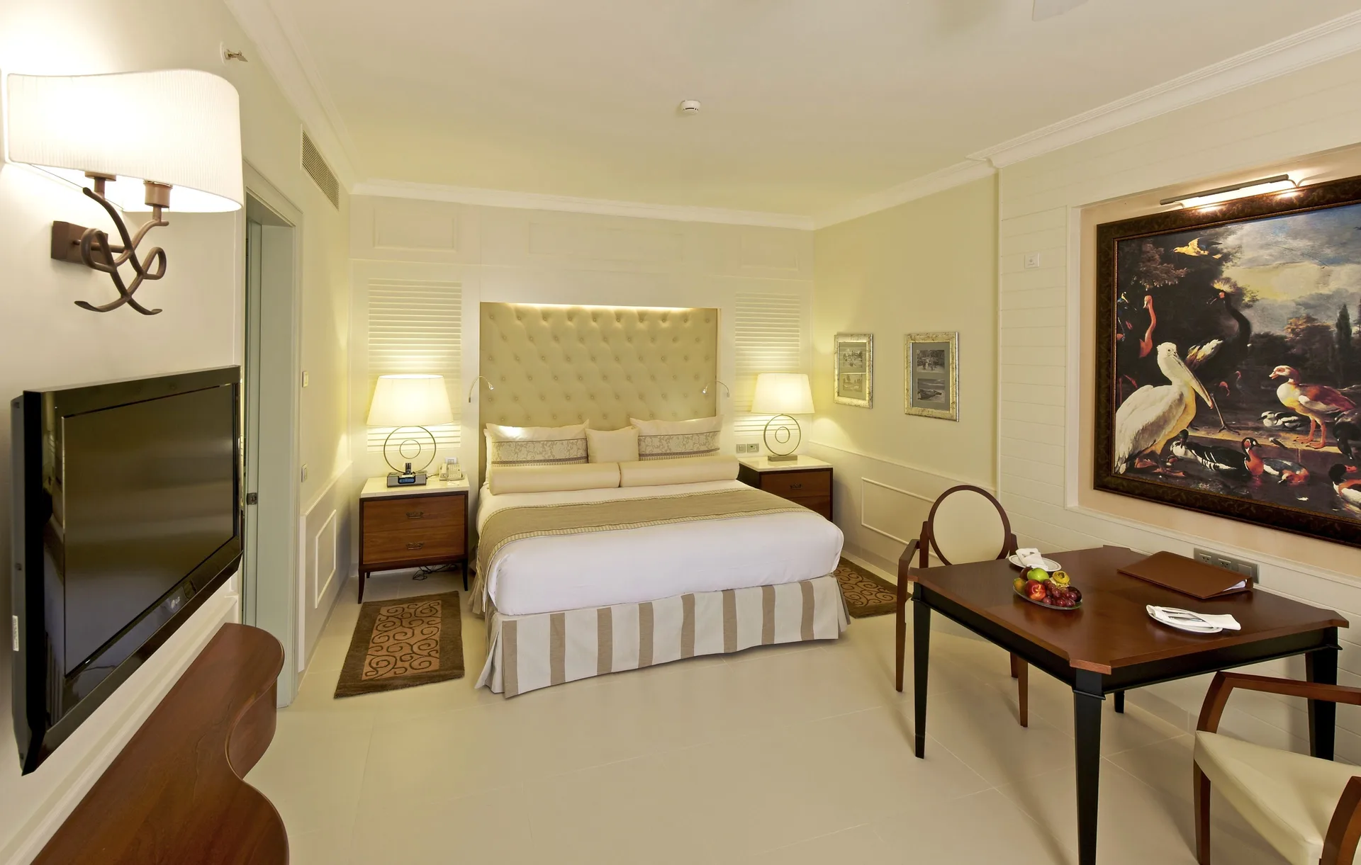 Suite bedroom with king bed, wall-mounted TV and dining table at JOIA Bávaro by Iberostar.