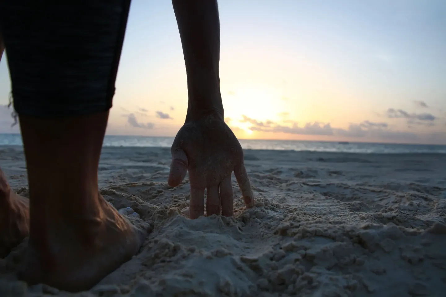 Hand and feet in beach sand at sunrise at JOIA Paraíso by Iberostar.