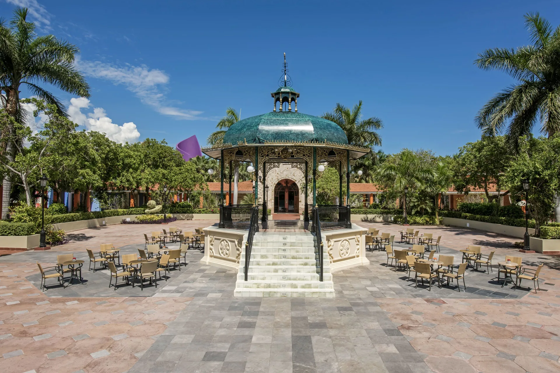 Central plaza gazebo at JOIA Paraíso by Iberostar surrounded by tables, palms, and tiled paving.