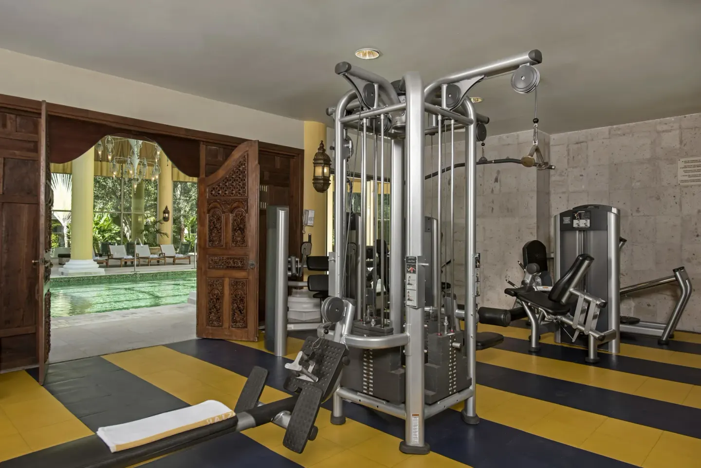 Fitness room with weight machines and open doors to the pool at JOIA Paraíso by Iberostar.