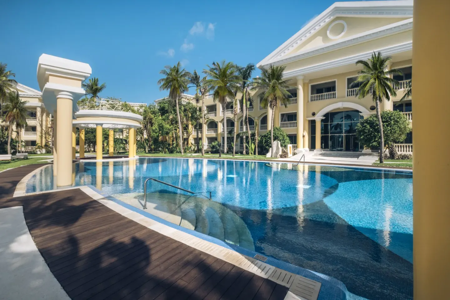 Pool beside yellow resort buildings and palms at JOIA Paraíso by Iberostar.