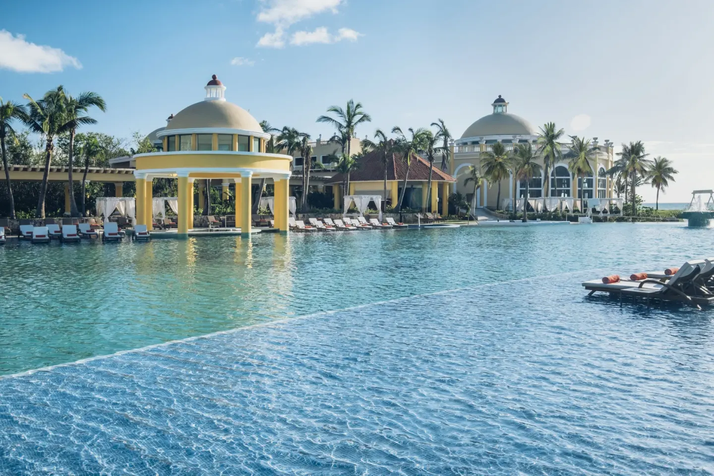 Wide blue pool with domed pavilions and palm trees at JOIA Paraíso by Iberostar.