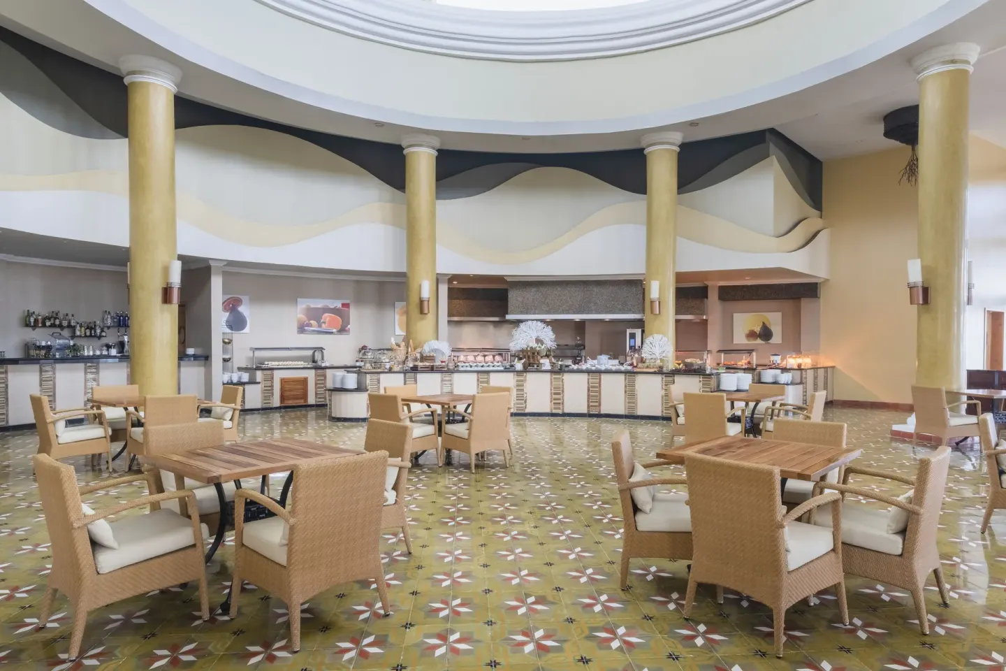 Buffet dining room at JOIA Paraíso by Iberostar with wicker chairs, wooden tables, and tall columns.