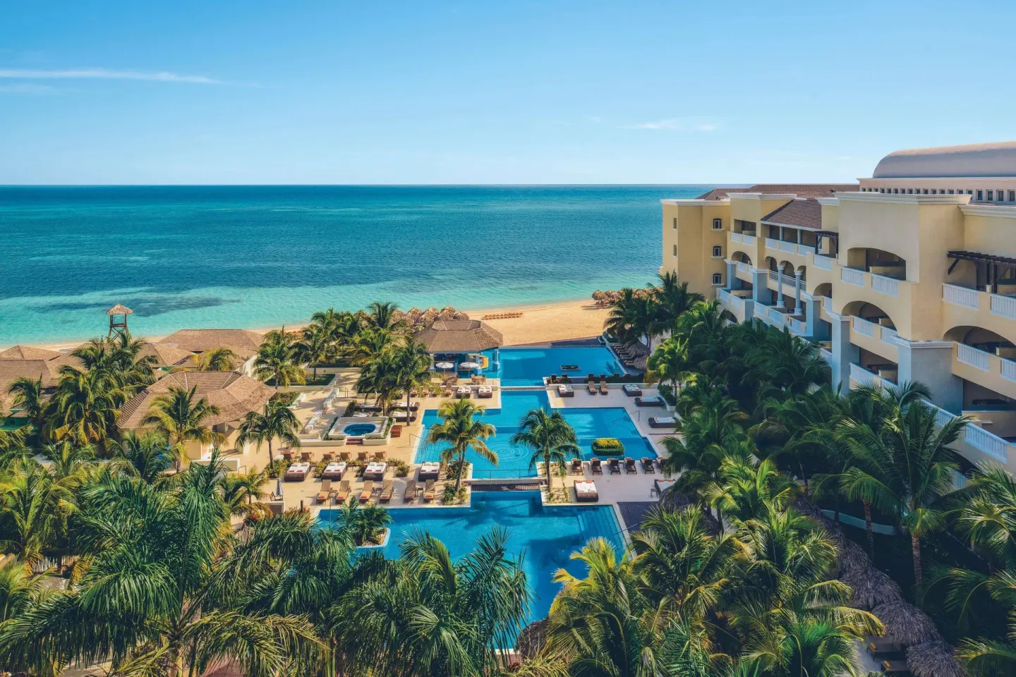 Aerial view of pools, palms, beach, and resort buildings at JOIA Rose Hall by Iberostar.