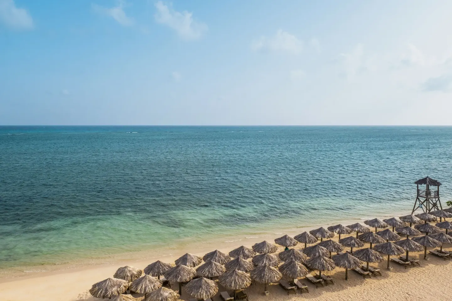 Beach palapas, loungers, and calm sea at JOIA Rose Hall by Iberostar.
