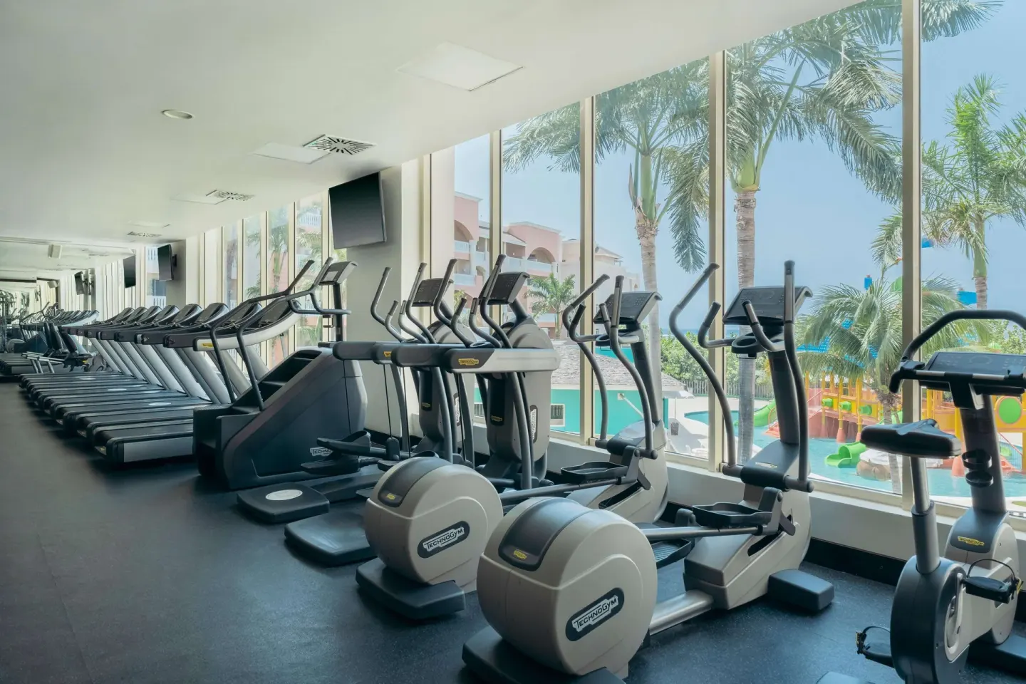 Cardio gym with treadmills and elliptical machines by windows at JOIA Rose Hall by Iberostar.