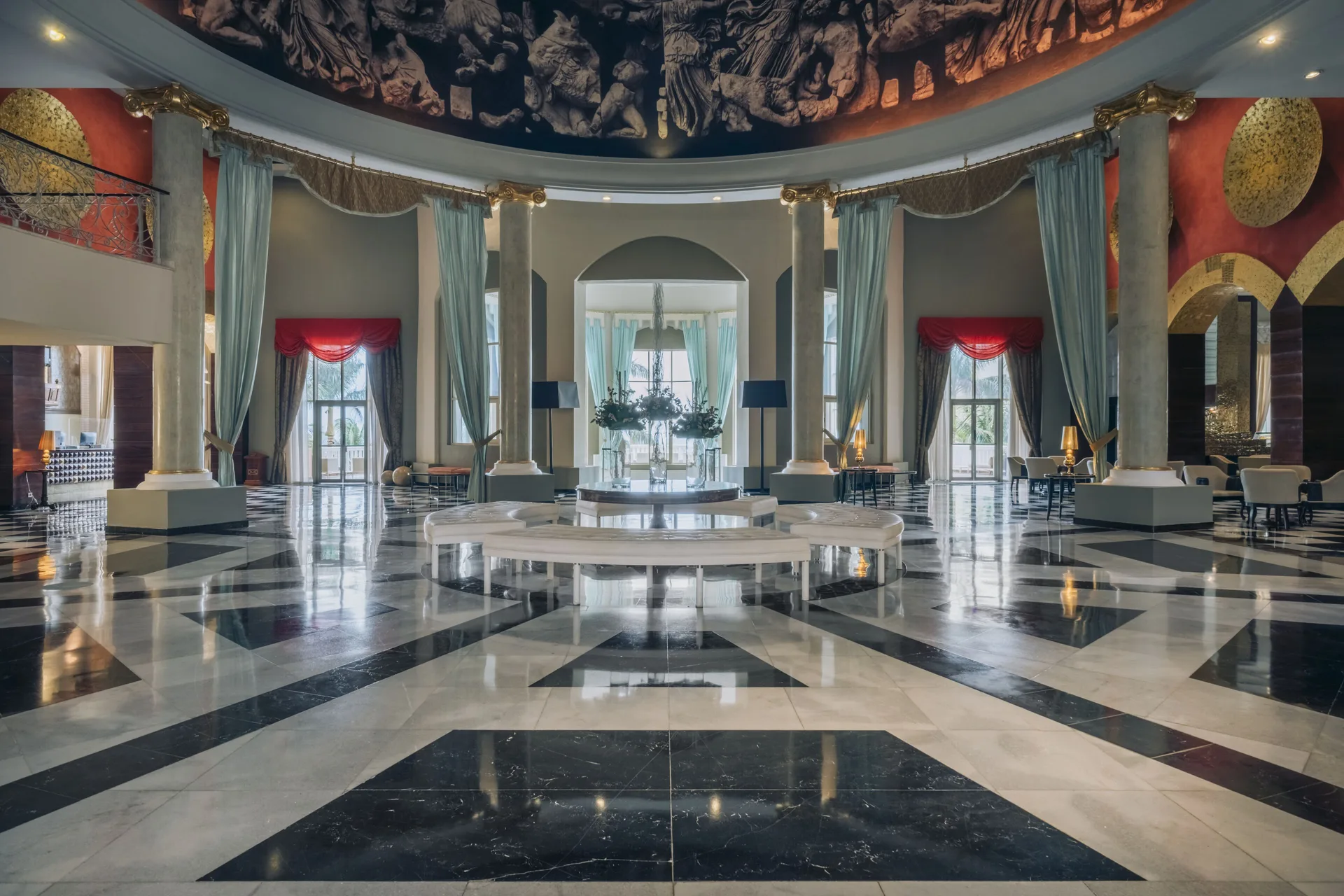 Circular lobby at JOIA Rose Hall by Iberostar with columns, draped windows, benches, and glossy marble floors.