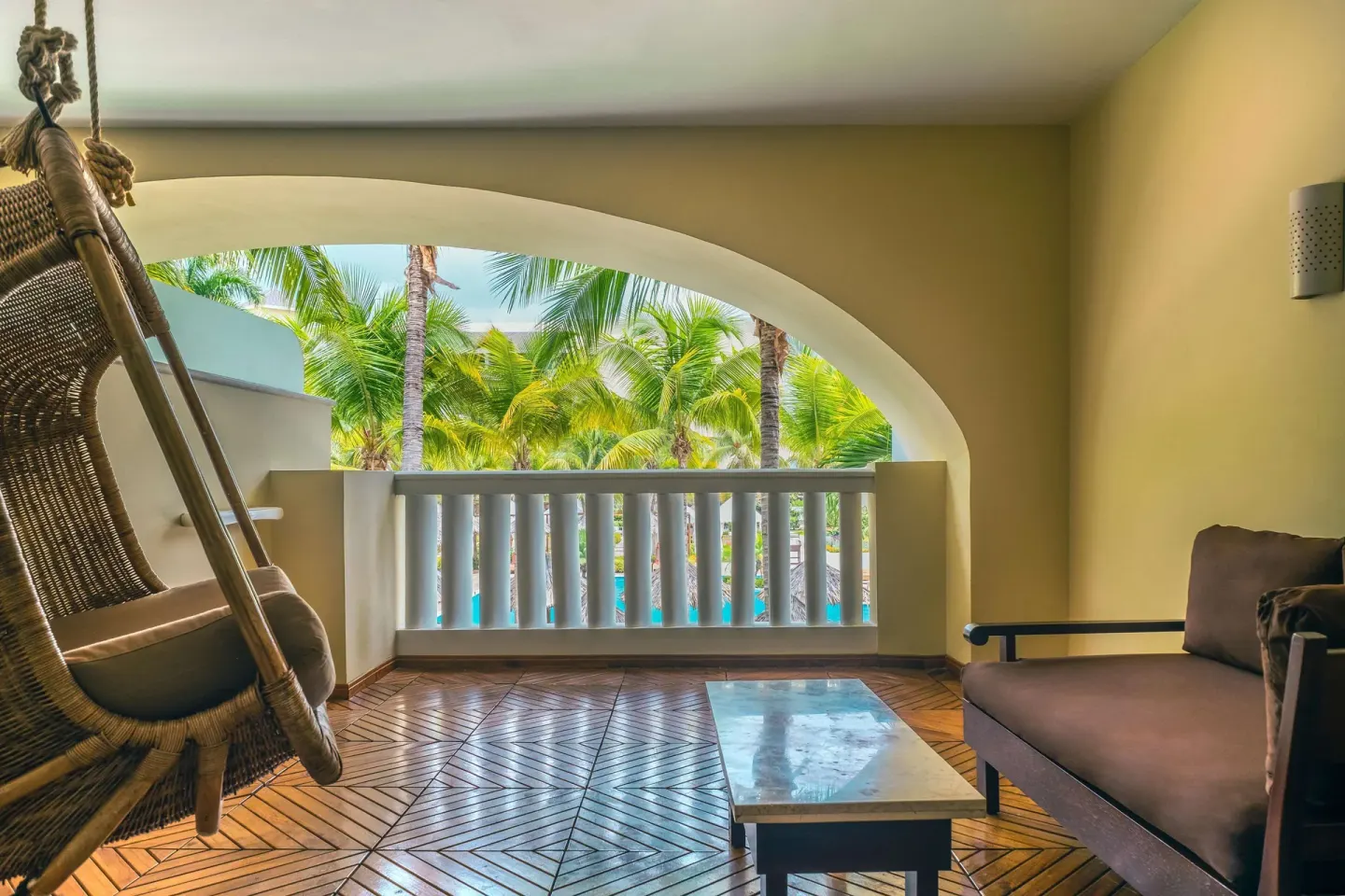 Covered balcony with hanging chair and palm views at JOIA Rose Hall by Iberostar.