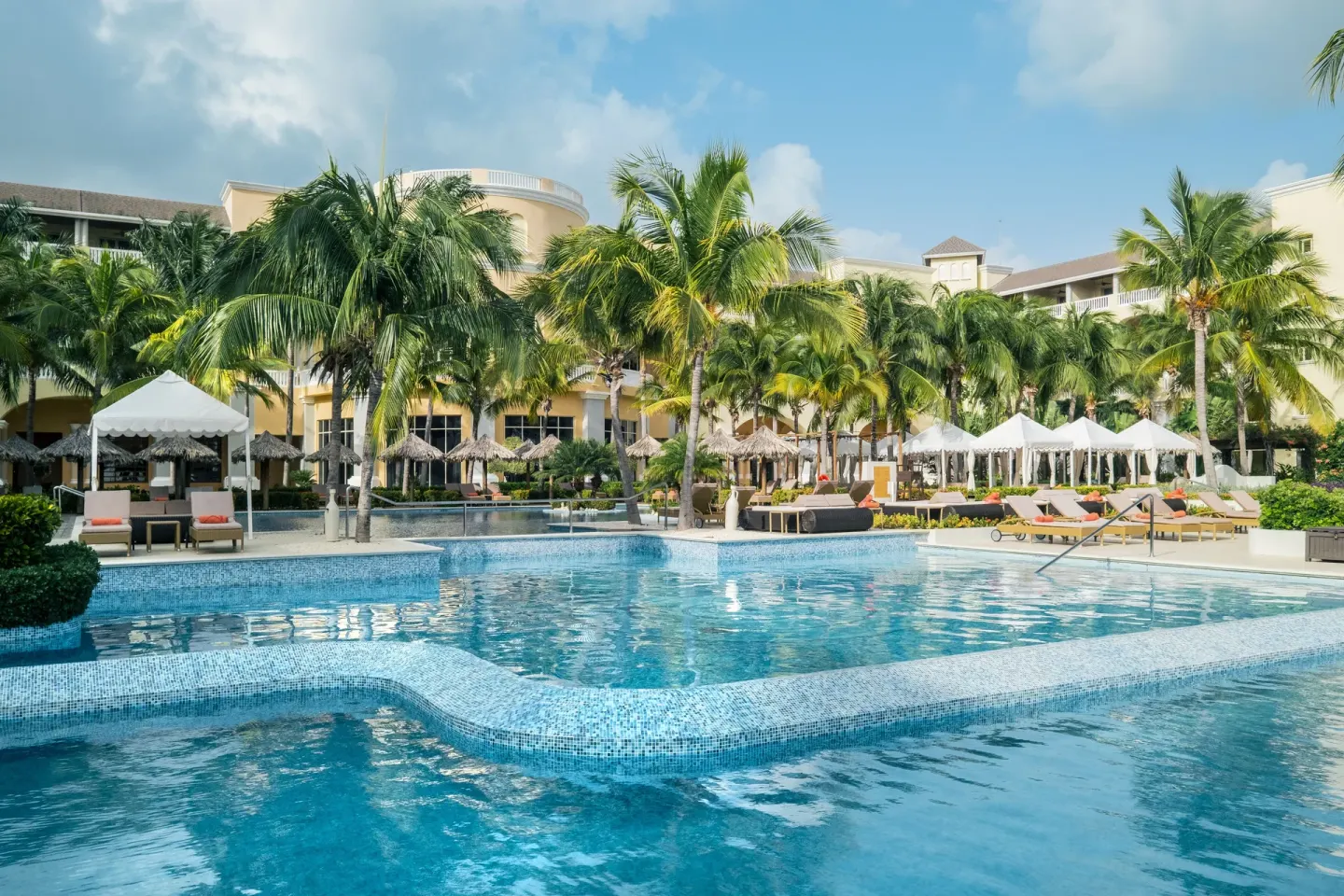 Curved resort pool with palms and sun loungers at JOIA Rose Hall by Iberostar.