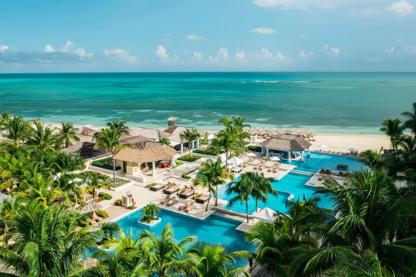 Elevated view of pools, palms, and beach at JOIA Rose Hall by Iberostar.