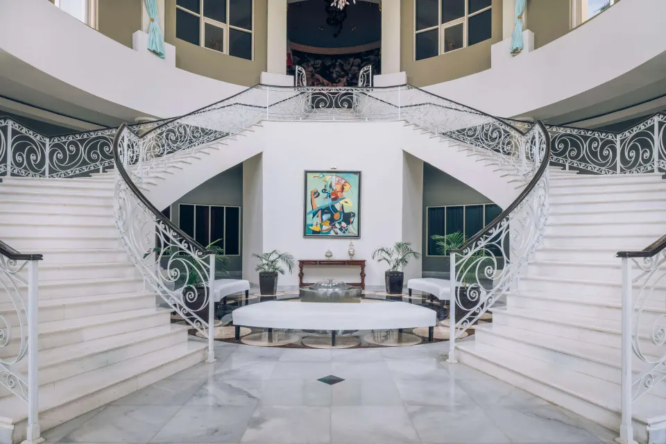 Grand white staircase at JOIA Rose Hall by Iberostar with ornate railings and a seating area below.