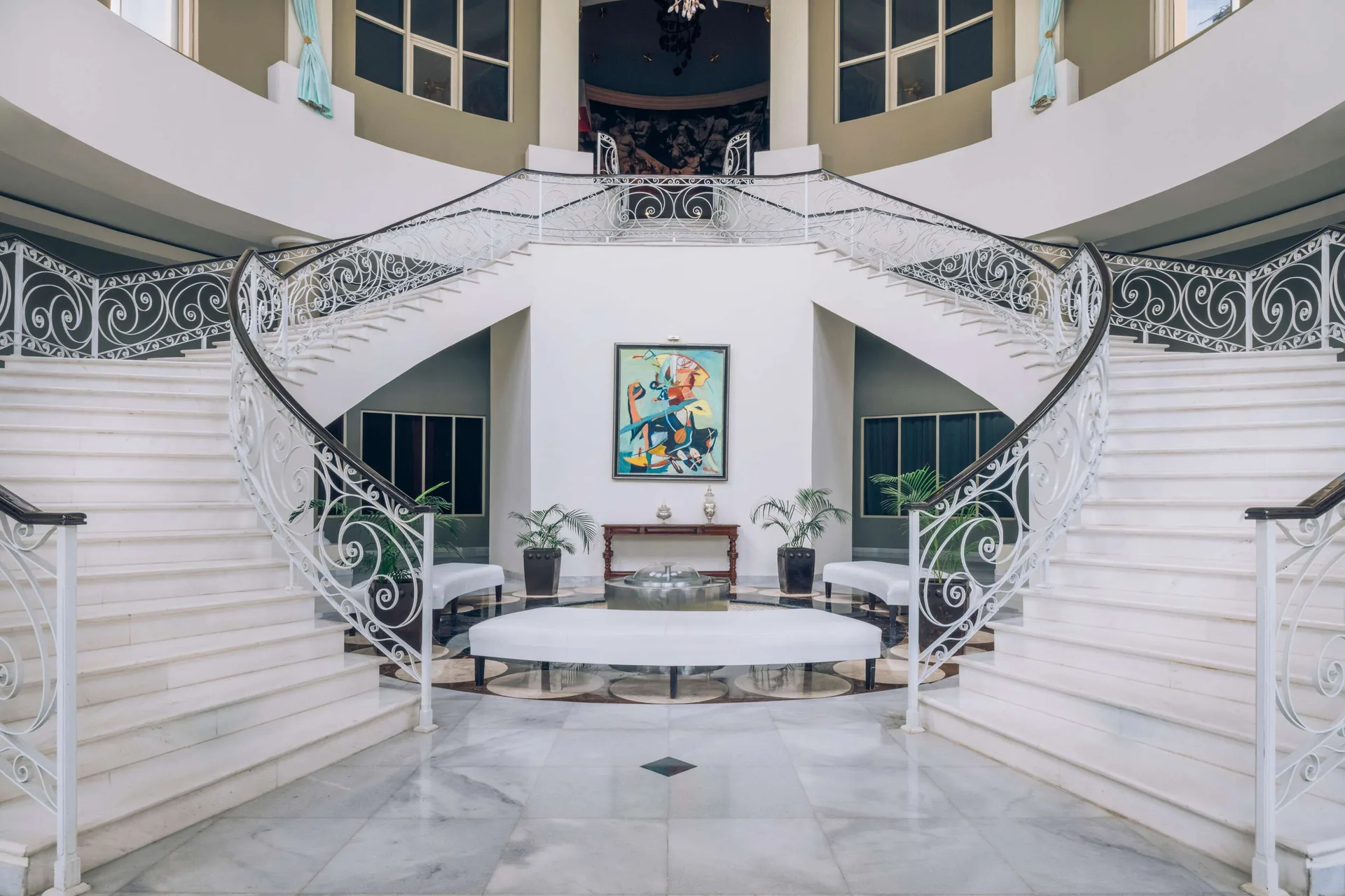 Grand white staircase at JOIA Rose Hall by Iberostar with ornate railings and a seating area below.