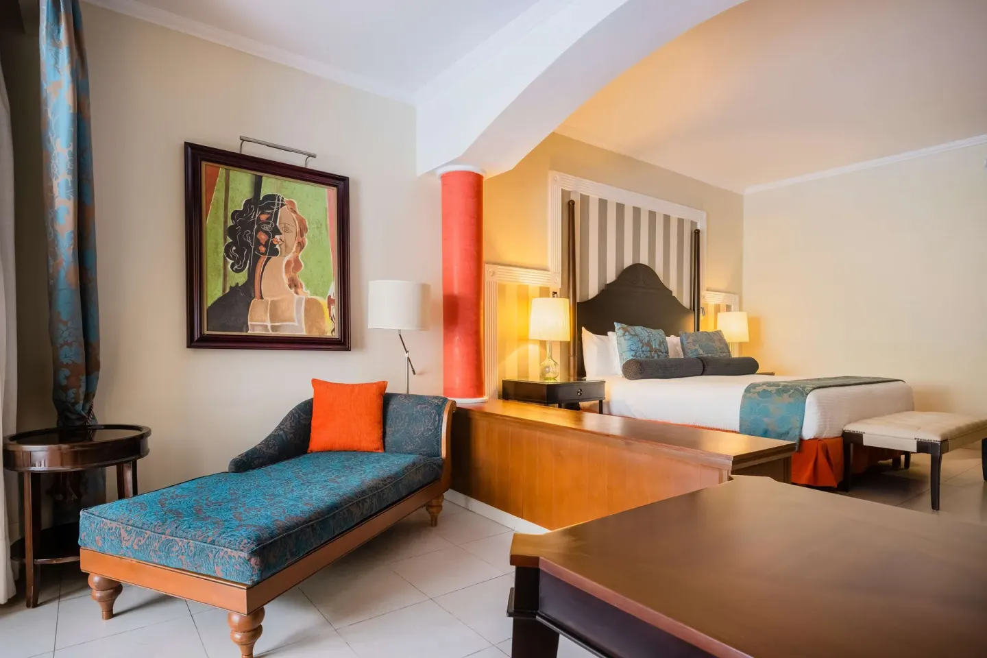 Guest room with king bed, chaise lounge, and portrait art at JOIA Rose Hall by Iberostar.