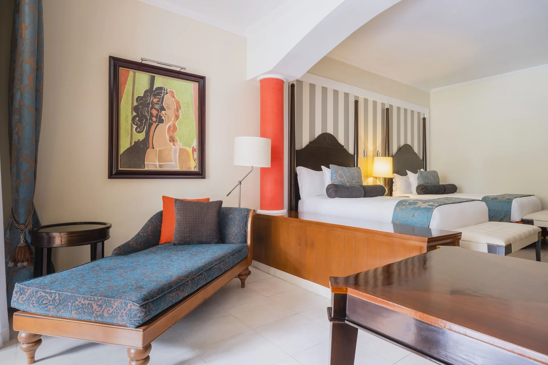 Guest room at JOIA Rose Hall by Iberostar with two beds, a chaise lounge, and framed art.