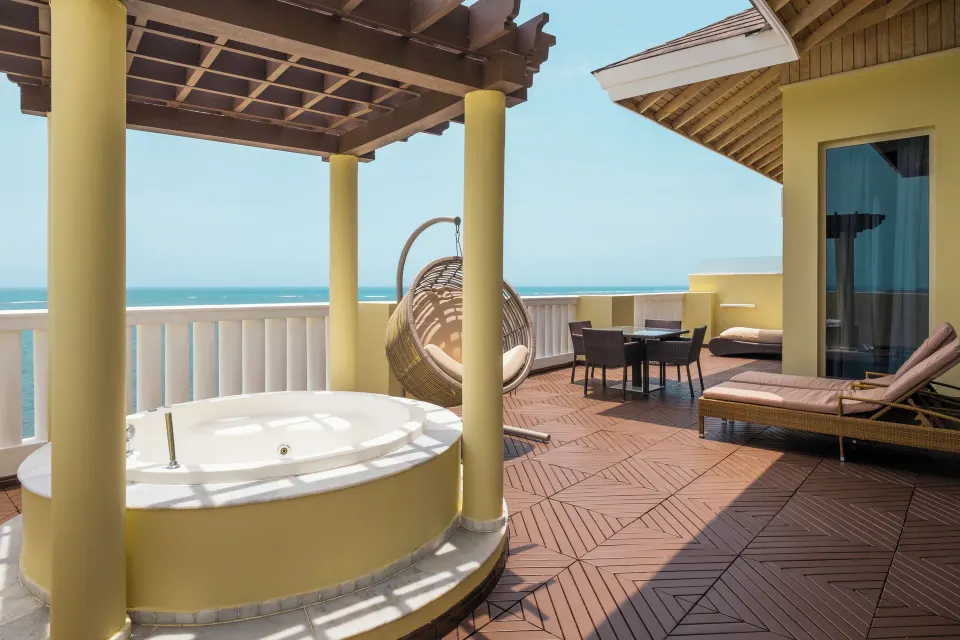 Ocean-view terrace at JOIA Rose Hall by Iberostar with a round soaking tub, hanging chair, loungers, and dining table.